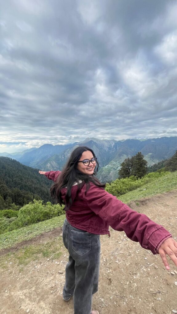 A traveller in a red jacket with her arms spread wide on a mountain trail