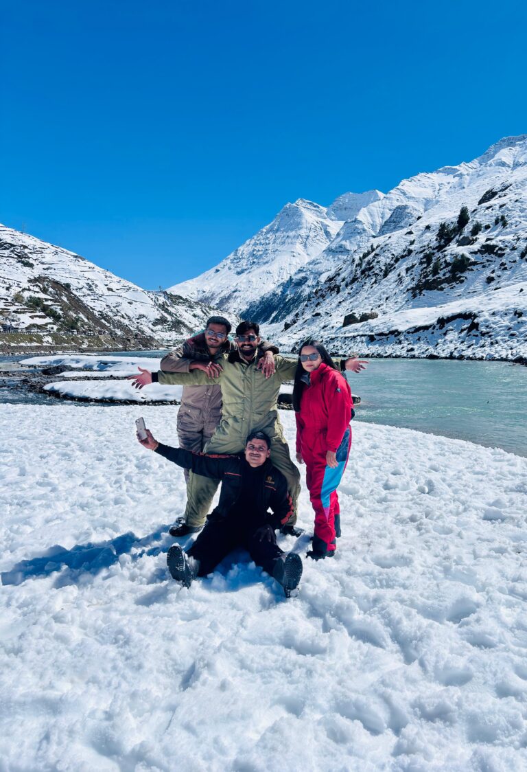 Friends playing in deep snow beside a frozen lake with snow-capped peaks behind