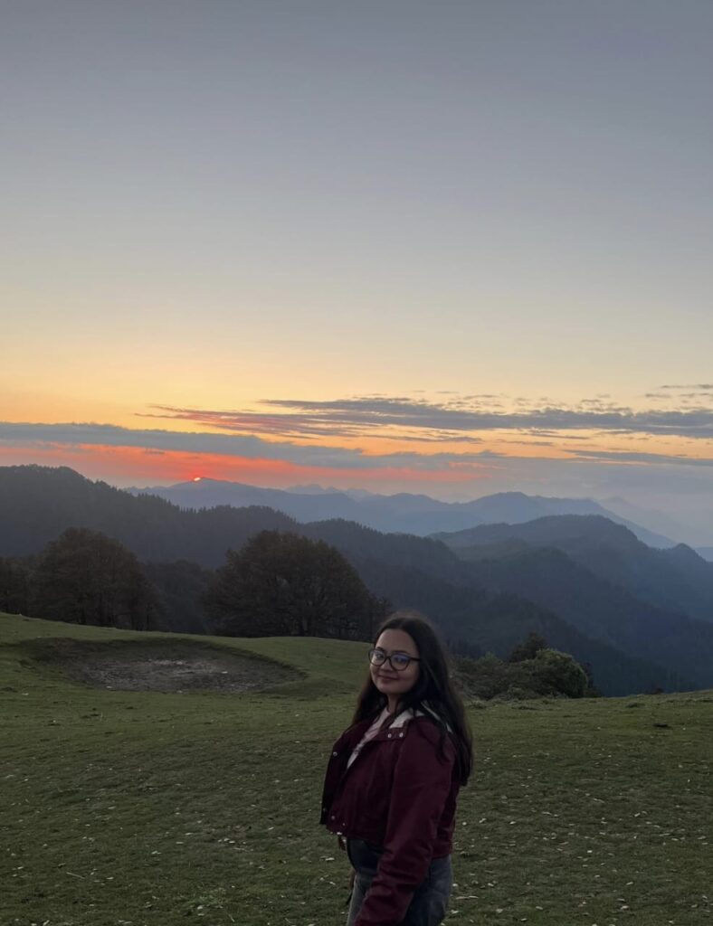 A traveller smiling on a mountain meadow as the sun sets behind the hills