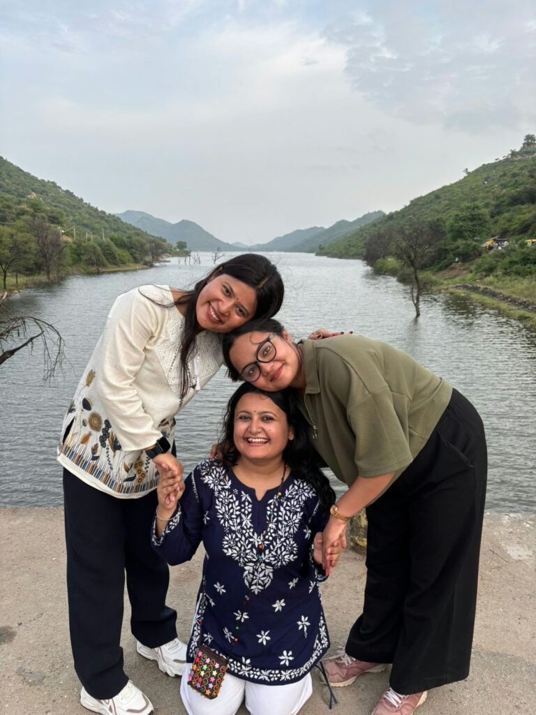 Three friends posing together beside a river in a green mountain valley