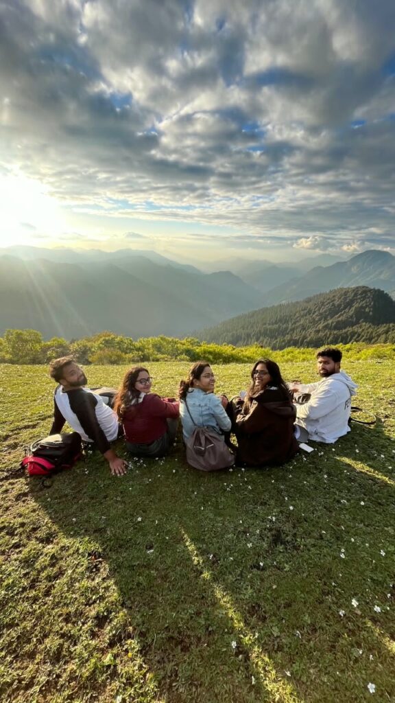 Yaarana Safar travellers sitting together on a green mountain meadow as the evening sun breaks through the clouds